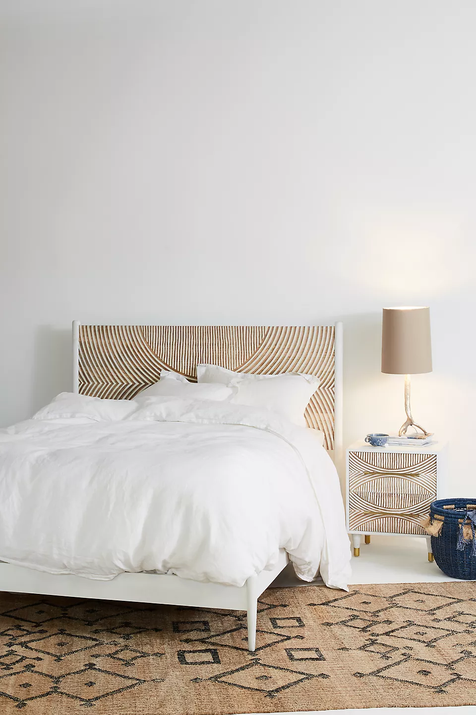A wooden white hand carved headboard. A bed with white bedding.