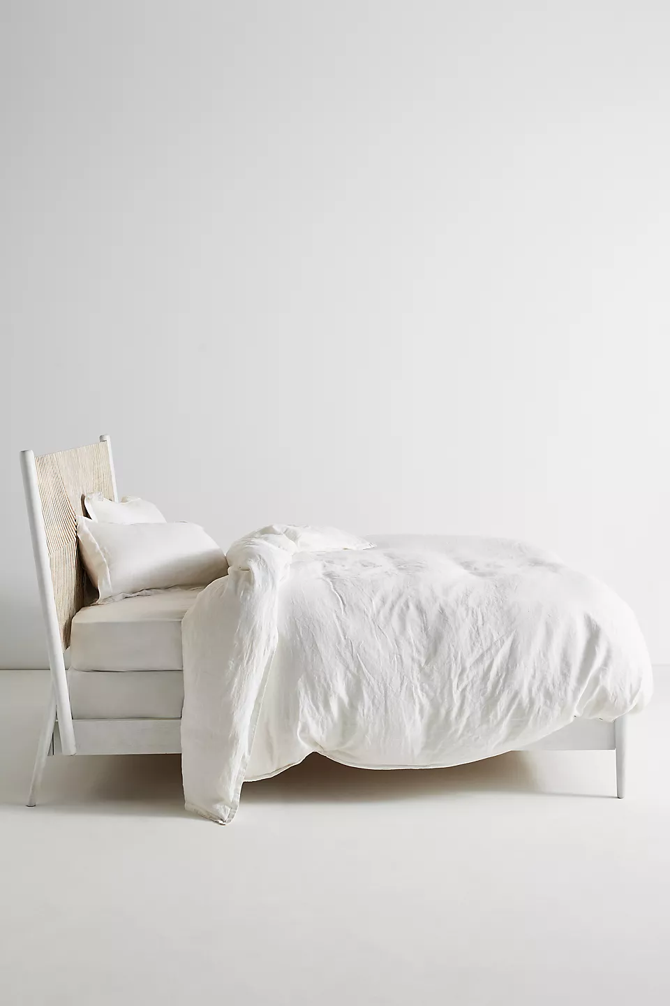 A wooden white hand carved headboard. A bed with white bedding.