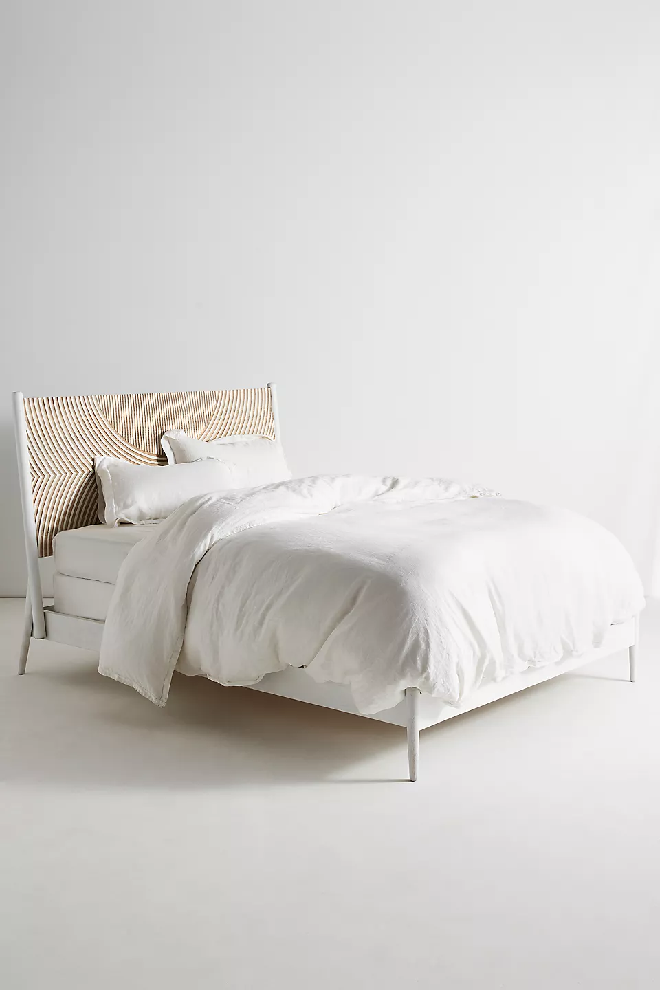 A wooden white hand carved headboard. A bed with white bedding.