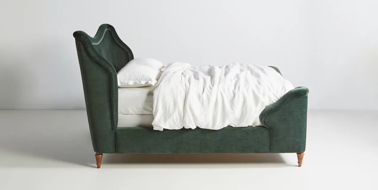 A green upholstered bed with white sheets on it.