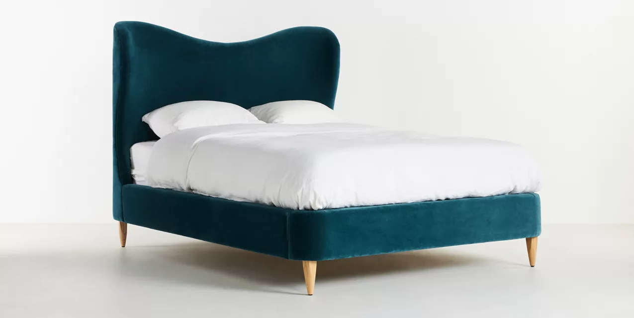 A bed with a blue velvet headboard and white bedding.