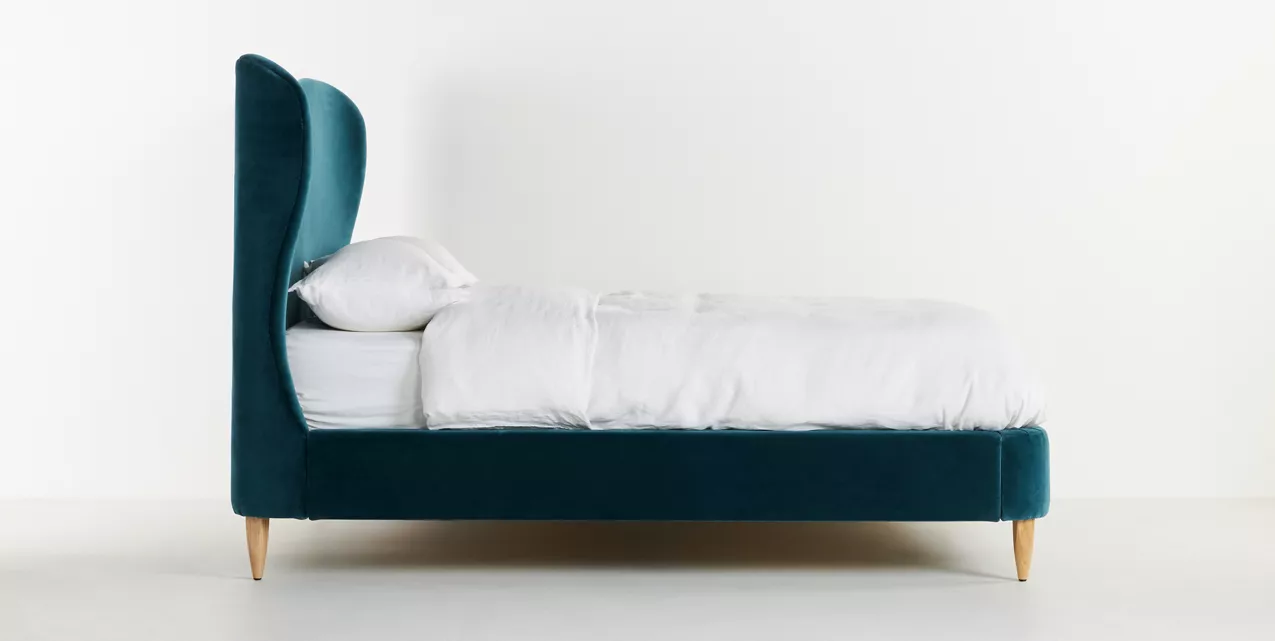 A bed with a blue velvet headboard and white bedding.