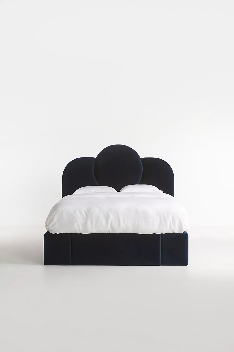 A bed with a blue velvet headboard and white bedding.