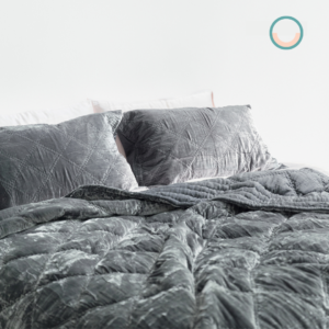 A bed with a grey silk velvet comforter and pillows.
