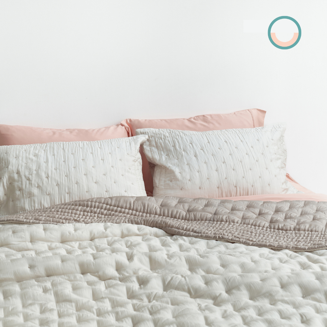 A bed with a white silk comforter and pink pillows.