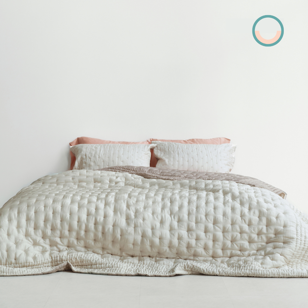 A bed with a white silk quilt and pink pillows.