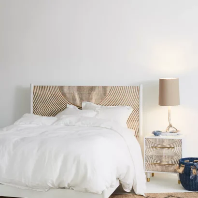 A wooden white hand carved headboard. A bed with white bedding.