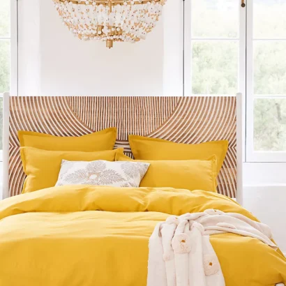 A wooden brown and white hand carved headboard. A bed with yellow bedding.