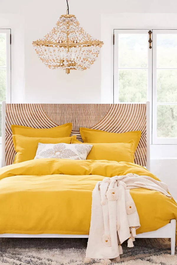 A wooden brown and white hand carved headboard. A bed with yellow bedding.