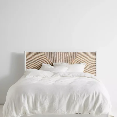 A wooden white hand carved headboard. A bed with white bedding.