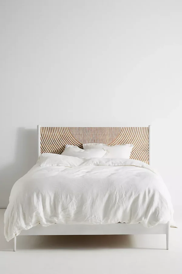 A wooden white hand carved headboard. A bed with white bedding.