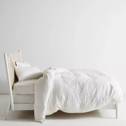 A wooden white hand carved headboard. A bed with white bedding.