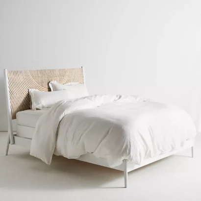 A wooden white hand carved headboard. A bed with white bedding.