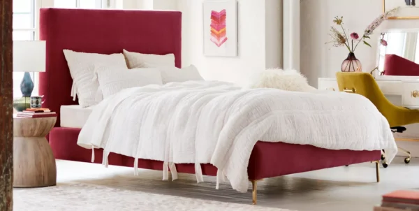 A bedroom with a burgundy upholstered bed. White Bedding.