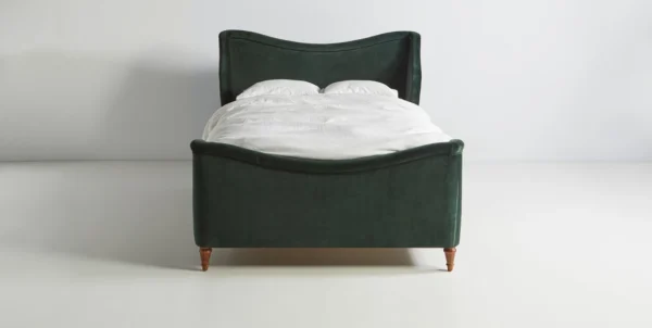 A green upholstered bed with white sheets on it.