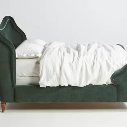 A green upholstered bed with white sheets on it.