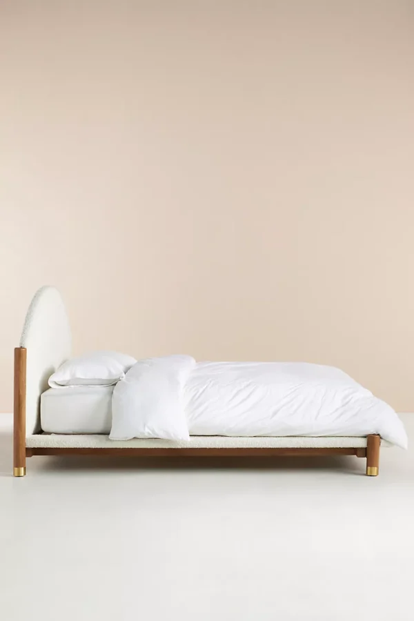 A bed with a wooden frame and a white upholstered headboard.