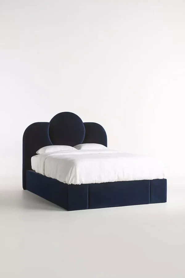 A bed with a blue velvet headboard and white bedding.