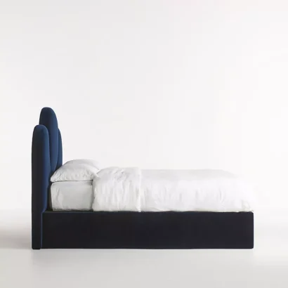 A bed with a blue velvet headboard and white bedding.