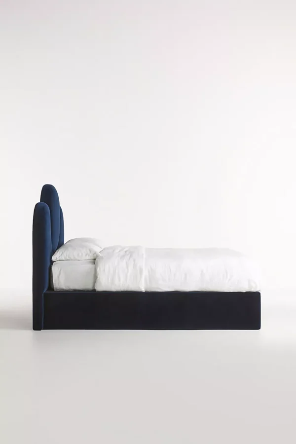 A bed with a blue velvet headboard and white bedding.