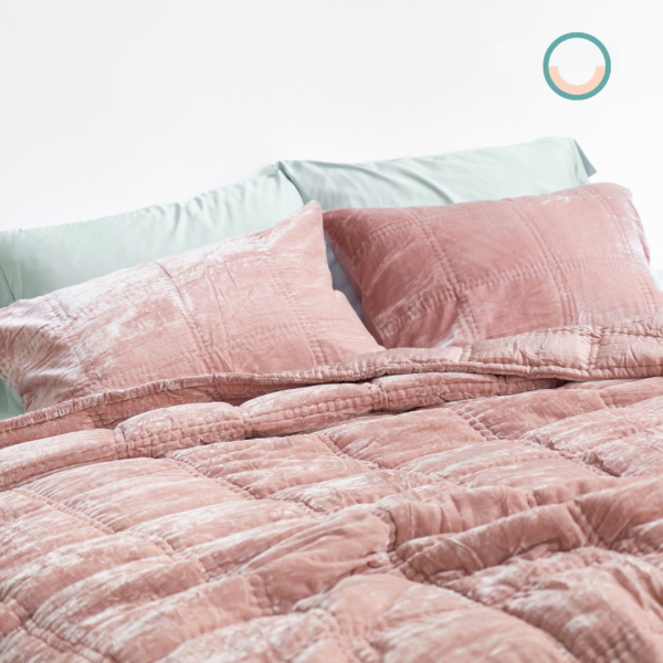 A bed with a pink silk velvet comforter and pillows.