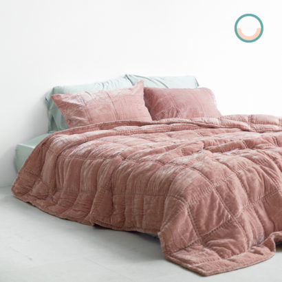 A bed with a pink silk velvet comforter and pillows.